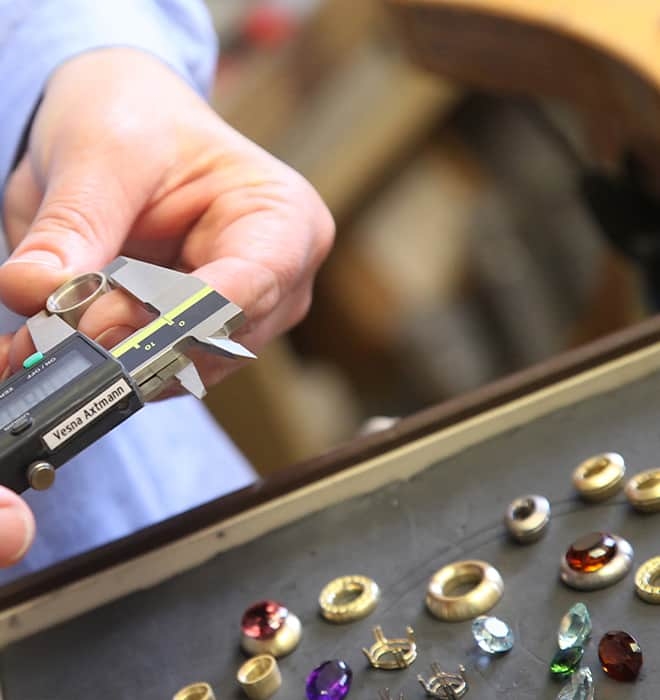Hand mit Schieblehre, Goldfassungen und Edelsteinen Meisteratelier